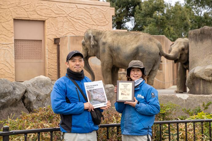 正田賞とZOO SCIENCE JOURNALを手にする職員の様子（かみね動物園象の前）