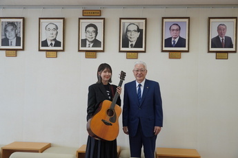 吉田正先生の写真の前で記念撮影をするおかゆさんと小川市長