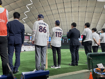 市長と德永社長の後ろ姿（ユニフォームの背番号）