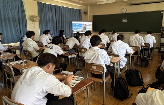 教室でメモを取り話を聞く生徒